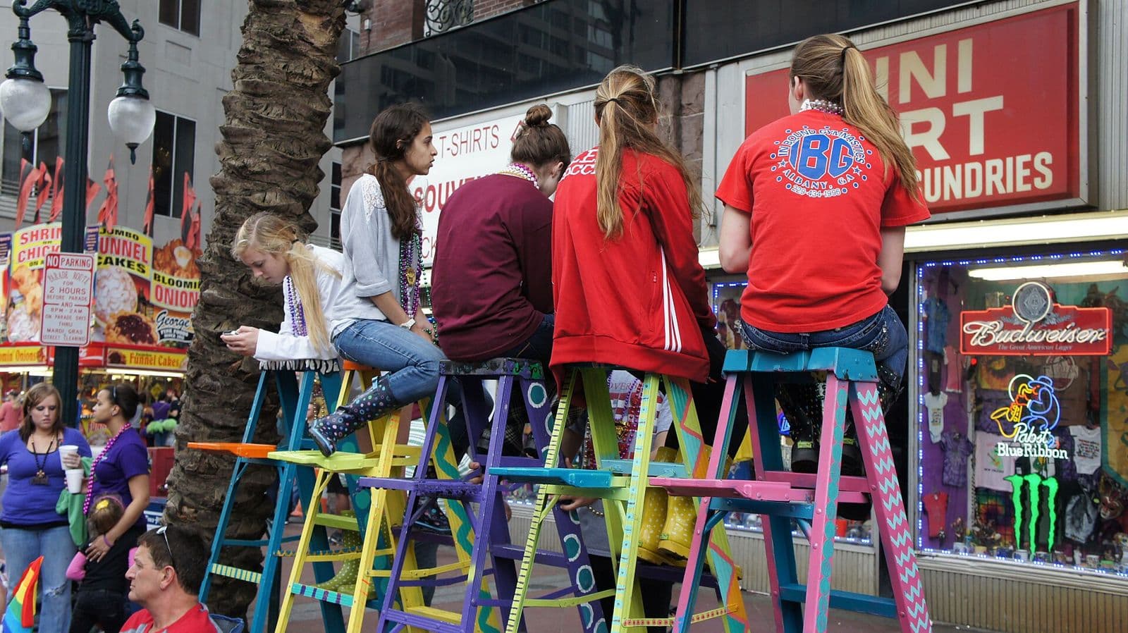 Young parade-goers sitting on colourful painted ladders on Canal Street, waiting for a Mardi Gras day parade