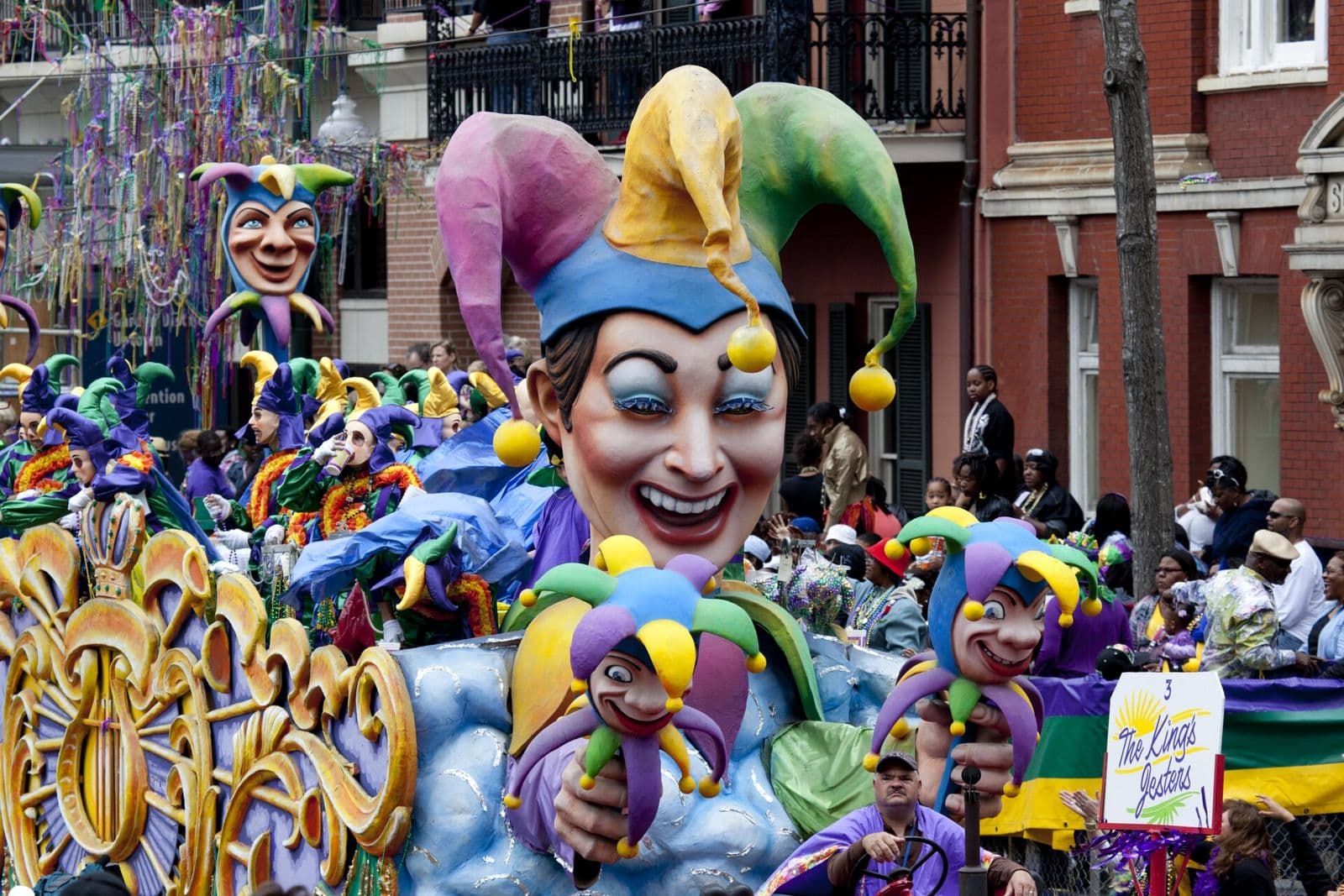 A giant smiling jester float with masked riders rolling through a New Orleans Mardi Gras parade