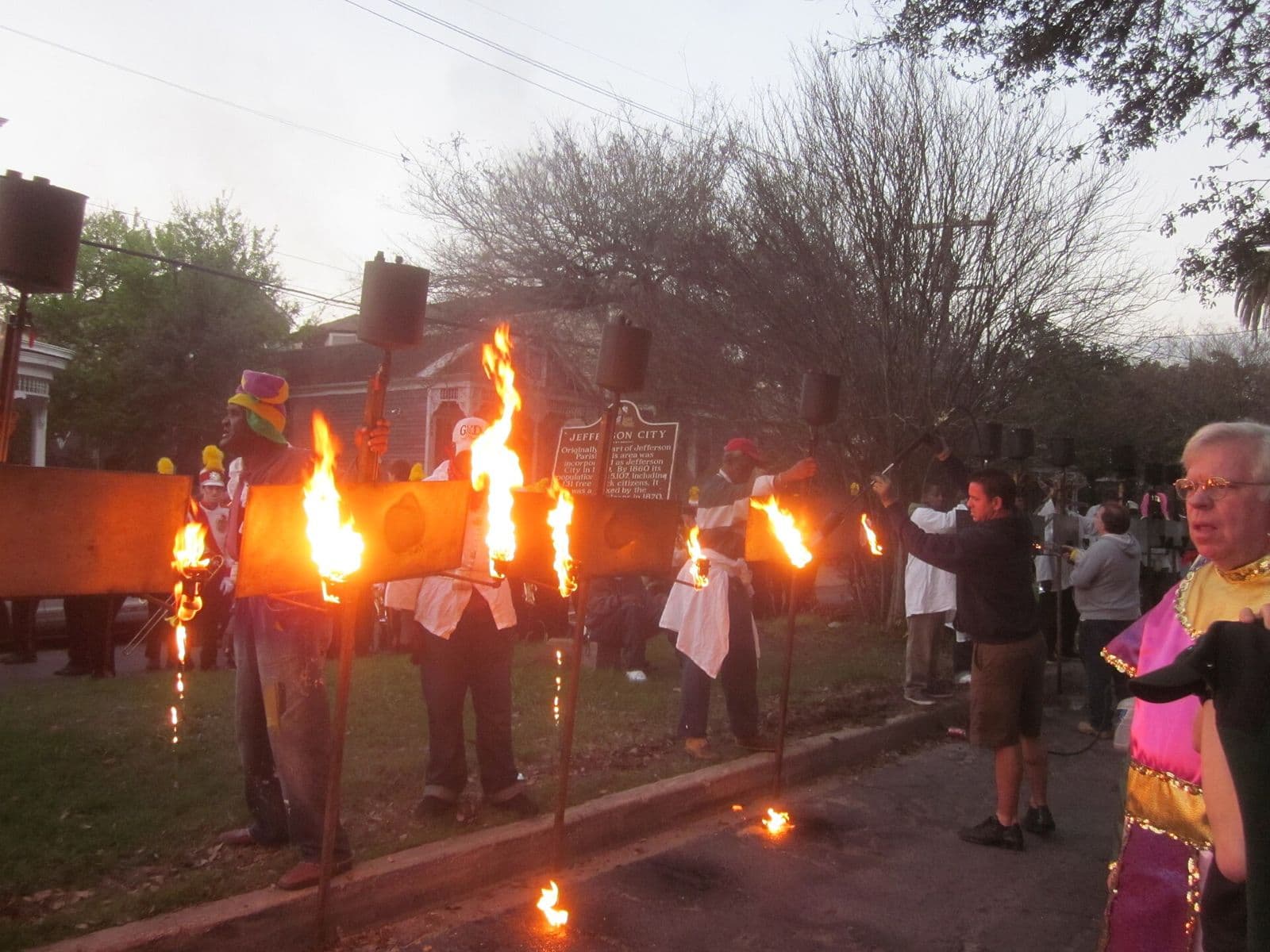 Flambeaux carriers lighting their torches at dusk on Jefferson Avenue before an Uptown night parade